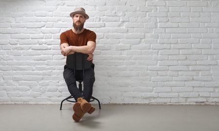 Bearded man sitting in front of white brick wallの写真素材
