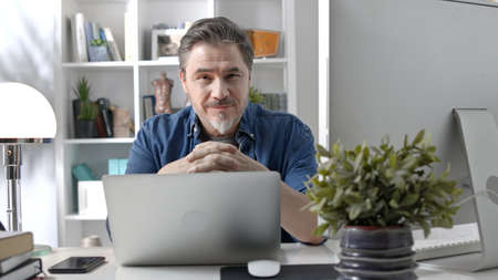 Portrait of happy older man in glasses at desk at homeの写真素材