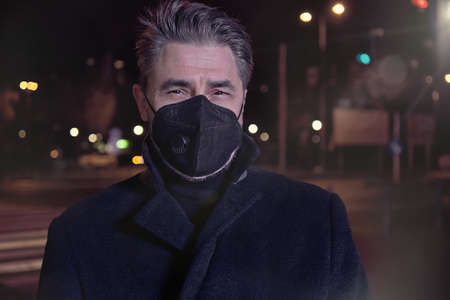 Covid-19 portrait - man in medical face mask on street at nightの写真素材