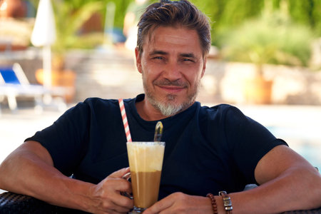 Man drinking ice coffee outdoor on vacation in hotel garden
