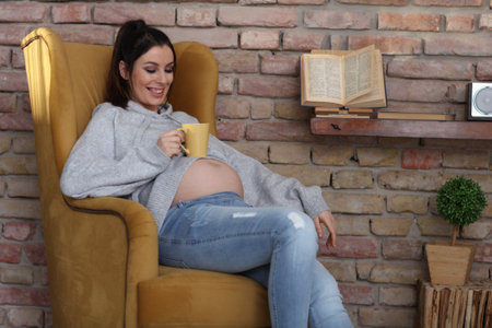 Happy pregnant woman at home relaxing in armchairの写真素材