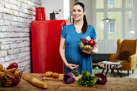 Pregnant woman at home in kitchen preparing saladの写真素材