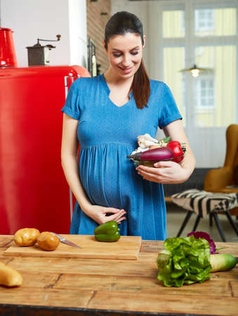 Pregnant woman at home in kitchen preparing saladの写真素材