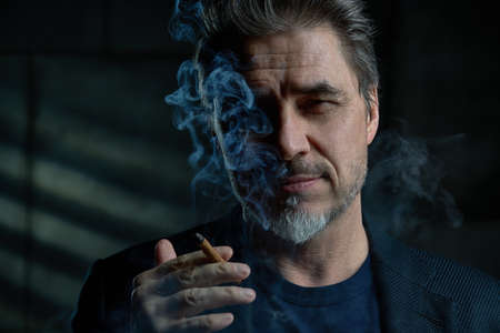 Portrait of middle aged man in dark smoking cigarの写真素材