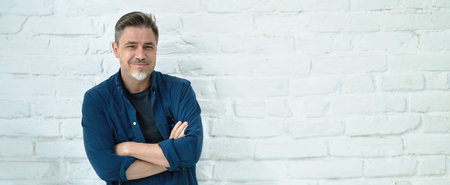 Portrait of happy casual middle aged man smiling. Copy space, white brick wall.