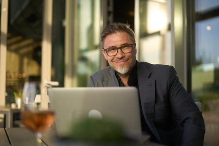 Happy businessman with laptop computer in restaurant. Middle aged man sitting at table in hotel lobby or business lounge in office, working, smiling.の写真素材