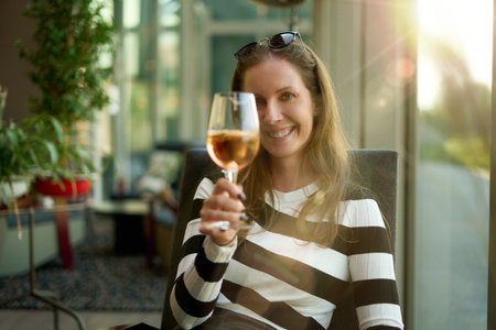 Woman sitting on cafe drinking champagne based cocktail from wine glass, smiling.の写真素材