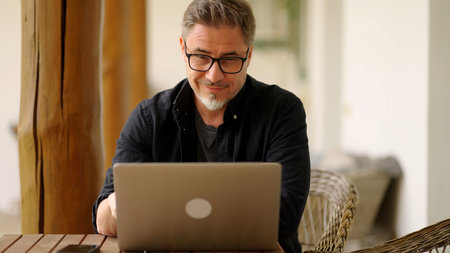 Businessman in home office. Middle aged man working with laptop computer at home outdoor on terrace. Online work, happy, smiling.の写真素材