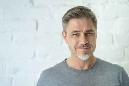 Portrait of happy casual middle aged man smiling. Copy space, white brick wall.