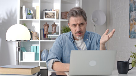 Older white man sitting at desk using laptop in home office. 50s businessman on video chat conference call and working from home.の写真素材