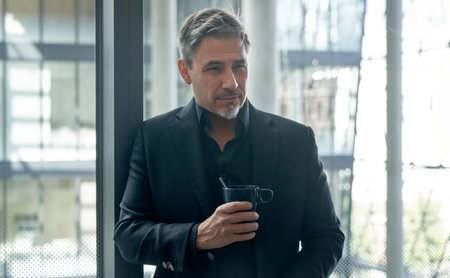 Business portrait - businessman drinking coffee in office, smiling. Mature age, middle age, mid adult man in 50s with gray hair and happy confident smile. Copy space.の写真素材