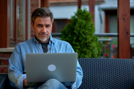 Outdoor portrait of mid adult man in 50s, happy confident smile. Working with laptop computer in home office. Mature age, middle age, bearded.の写真素材