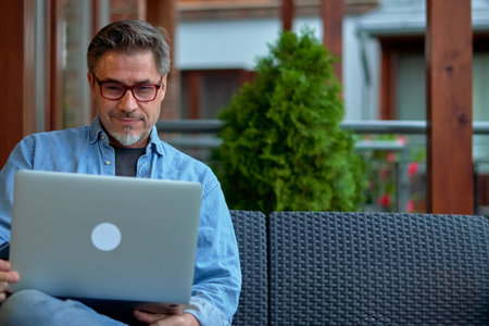 Outdoor portrait of mid adult man in 50s, happy confident smile. Working with laptop computer in home office. Mature age, middle age, bearded.の写真素材