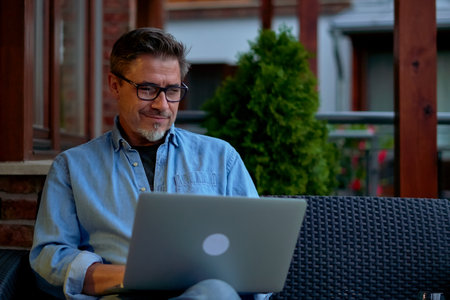 Outdoor portrait of mid adult man in 50s, happy confident smile. Working with laptop computer in home office. Mature age, middle age, bearded.の写真素材