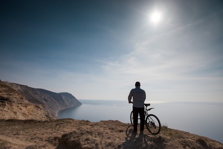 A cyclist stands on the high seashoreの写真素材