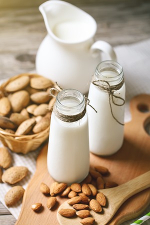Almond and almond milk on a wooden table in the summer garden. Useful food.の写真素材