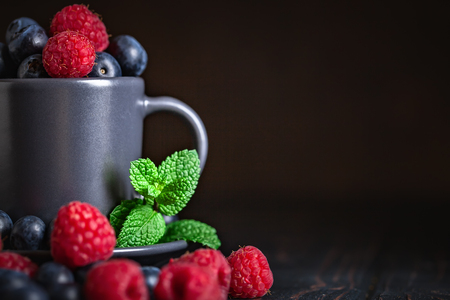 Raspberries and blueberries in a Cup on a darkの写真素材