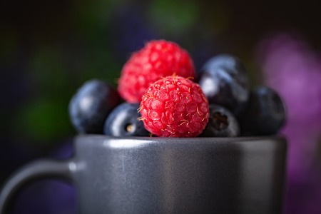 Raspberries and blueberries in a Cup on a darkの写真素材