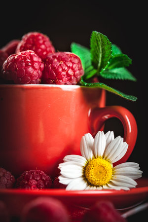 Raspberry in a red cup with chamomile and leaves on a dark