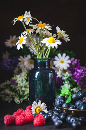 Raspberries and blueberries with chamomile and leaves on a dark background. Summer and healthy food concept. Selective focus.の写真素材