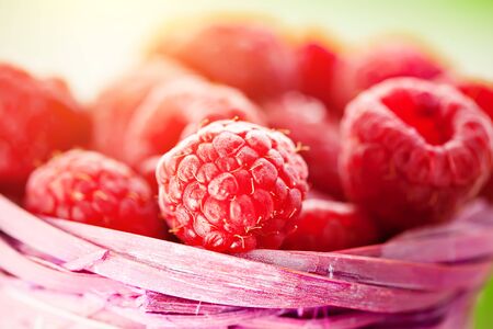 Fresh raspberries in a basket on a wooden table in the garden. Summer and healthy food concept. Selective focus.の写真素材