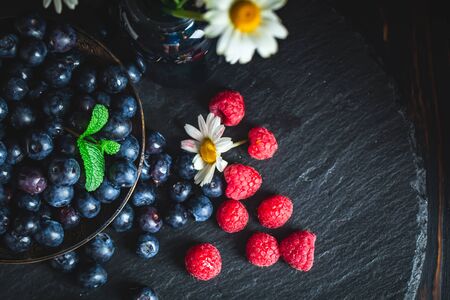 Raspberries and blueberries with chamomile and leaves on a dark background. Summer and healthy food concept. Selective focus. Horizontal.の写真素材