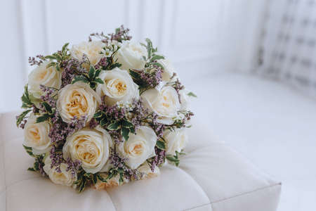 close-up of a wedding bouquet of cream roses with purple flowers lies on a white sofa in a bright roomの写真素材