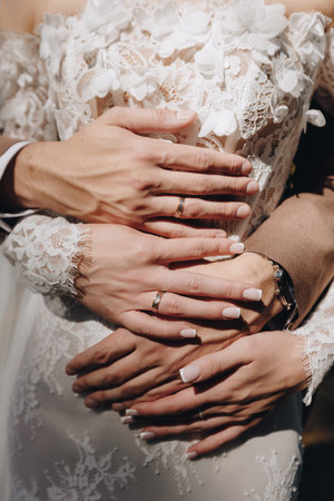 Bride and groom's hands with wedding rings holding each other gently, detailed lace dress highlights...