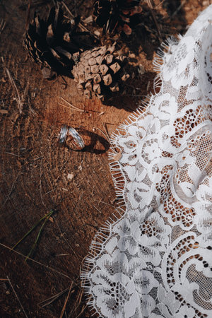 Wedding rings with pinecones and white lace on wooden background, reflecting rustic outdoor ceremony and natural elegance.の写真素材