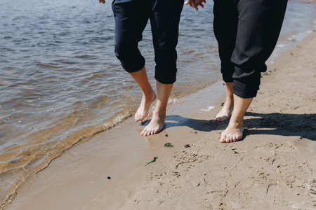 Barefoot couple walks side by side along the sand and waterline, enjoying nature and the feeling of freedom and closeness on a sunny dayの写真素材