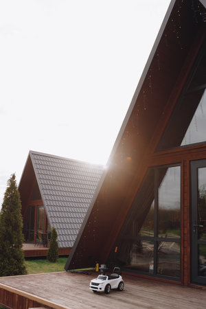 Contemporary A-frame house with large windows and a wooden deck in a scenic countryside setting at sunset.の写真素材
