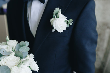 Elegant groom wearing a navy blue suit and bow tie, with a white flower boutonniere and wedding bouquet, ready for the wedding ceremony and celebration.の写真素材