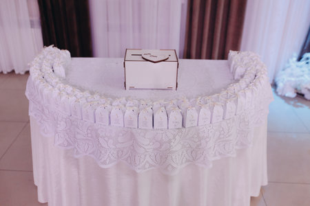 Row of neat wedding favor boxes with delicate ribbons and thank you notes, closeup detail of celebration decor on white lace tablecloth.の写真素材