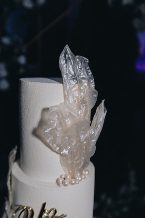 Closeup of edible sugar pearls and transparent sugar leaves on a white wedding cake, highlighting creative pastry decoration and artistry.の写真素材