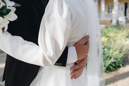 Bride and groom hugging close with white lilies bouquet in hand, romantic wedding moment outdoors...