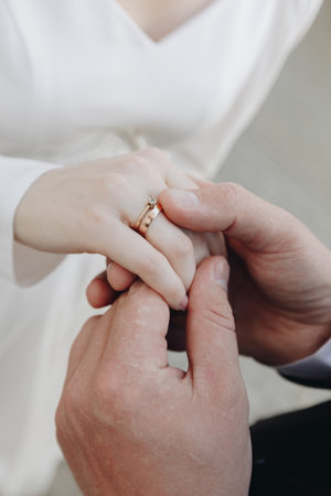 Bride and groom hold hands, their wedding rings visible, symbolizing unity, commitment and love on their special day.の写真素材