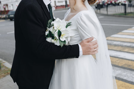 Groom in suit holding elegant bouquet of white flowers, natural background, stylish detail from wedding celebration.の写真素材