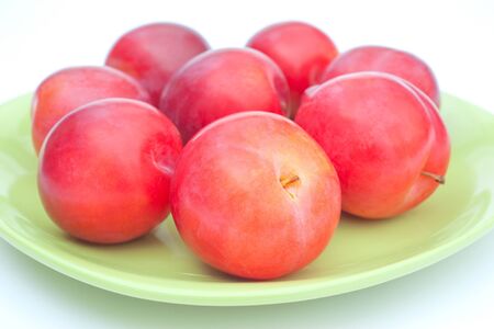 Ripe red plums on green plate on white backgroundの写真素材