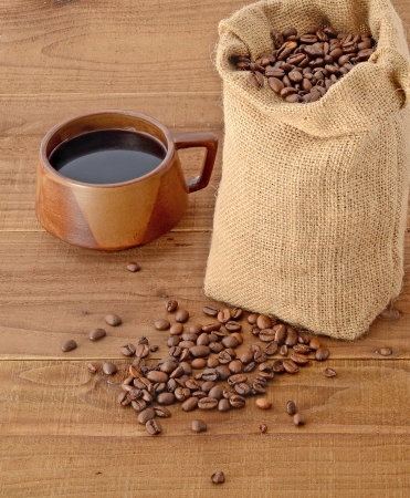Coffee beans in a sack on  wooden surface and a cup of coffeeの写真素材