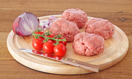 Raw meat homemade burgers with onion and tomatoes on wooden boardの写真素材