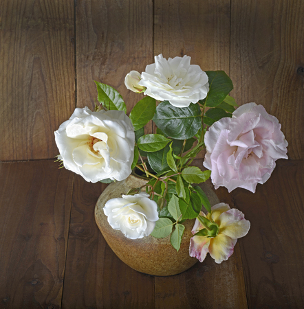 white and pink roses in the ceramic vase on the wooden surfaceの写真素材