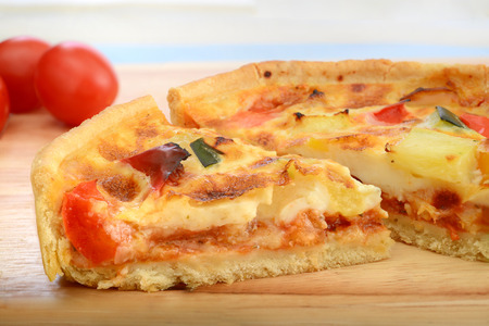 slice of grilled quiche and tomatoes on wooden cutting boardの写真素材
