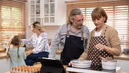 Multi-generational family members explore new and tasteful recipes on a tablet, make healthy food choices, cook, and enjoy meals together. Family gatherings help renew and strengthen relationships.の写真素材
