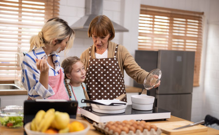 Multi-generational family members explore new and tasteful recipes on a tablet, make healthy food choices, cook, and enjoy meals together. Family gatherings help renew and strengthen relationships.の写真素材