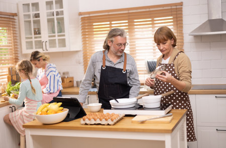 Multi-generational family members explore new and tasteful recipes on a tablet, make healthy food choices, cook, and enjoy meals together. Family gatherings help renew and strengthen relationships.の写真素材