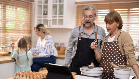 Multi-generational family members explore new and tasteful recipes on a tablet, make healthy food choices, cook, and enjoy meals together. Family gatherings help renew and strengthen relationships.の写真素材