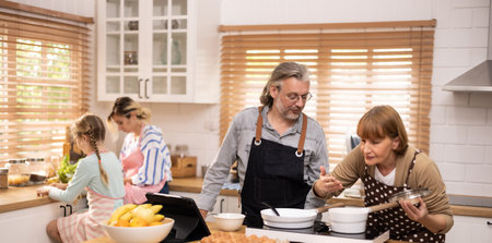 Multi-generational family members explore new and tasteful recipes on a tablet, make healthy food choices, cook, and enjoy meals together. Family gatherings help renew and strengthen relationships.の写真素材