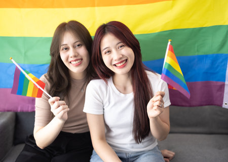 Shot of lovely Asian lesbian couples hold and wave tiny LGBT flags while smiling, being confident, and feeling proud. Actions that are both lively and harmonious showing gender equality in societyの写真素材