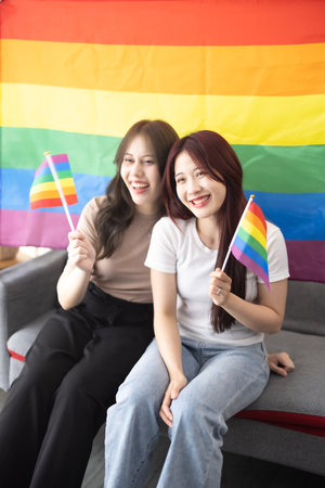 Shot of lovely Asian lesbian couples hold and wave tiny LGBT flags while smiling, being confident, and feeling proud. Actions that are both lively and harmonious showing gender equality in societyの写真素材