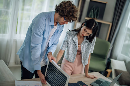 Startup team assess efficiency in renewable resource usage. Calculate cost saving for sustainable housing improvements, like solar panels. Plan eco-friendly changes, conscious electricity consumptionの写真素材